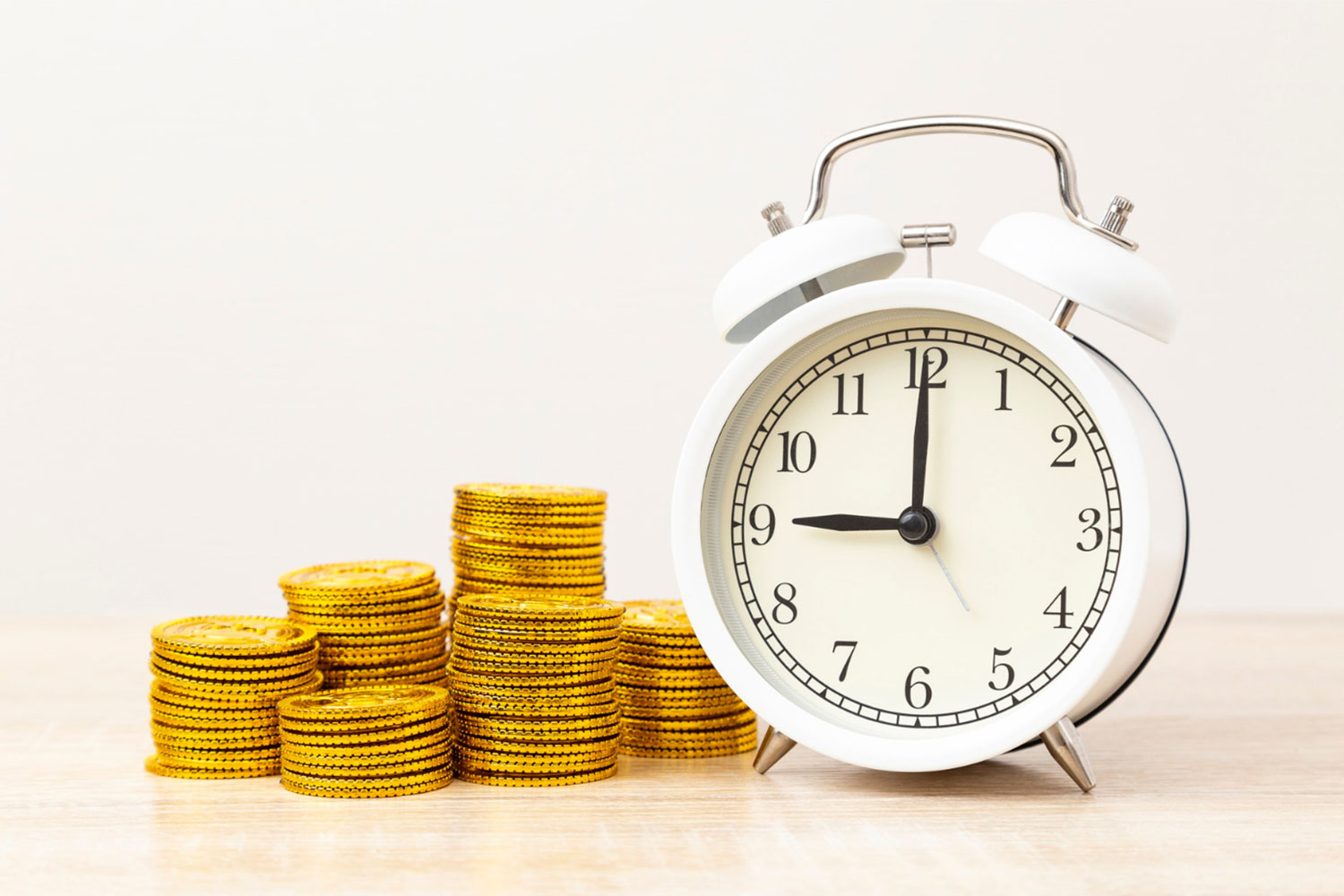 An alarm clock next to a stack of gold coins
